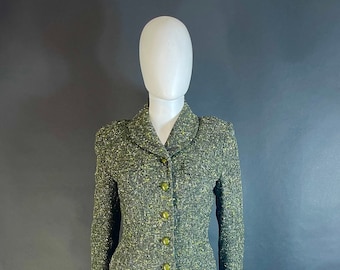 May include: A green and gold tweed skirt suit with a fitted jacket and a skirt with pleats. The jacket has a collar and five gold buttons.