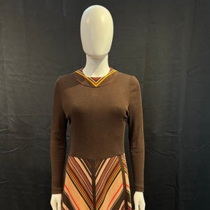 May include: A brown long-sleeved dress with a striped skirt. The skirt has brown, beige, orange, and red stripes.