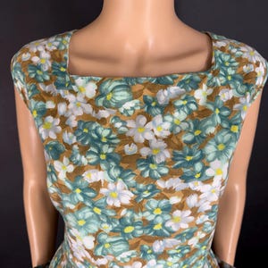 May include: A vintage floral dress with a square neckline. The dress features a brown background with a pattern of white, teal, and yellow flowers. The dress has a fitted bodice and a flared skirt, and is displayed on a mannequin.