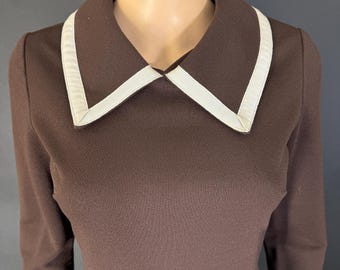 May include: A brown dress with a white collar and long sleeves. The collar has a wide white trim.