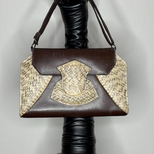 May include: A brown leather handbag with a snakeskin pattern on the front flap. The bag has a long strap and a top closure.