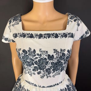 May include: A white dress with a black floral print. The dress has a square neckline and short sleeves. The skirt is full and gathered.