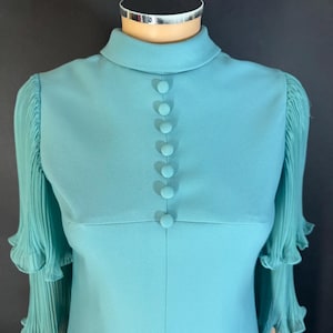 May include: A vintage turquoise dress with a high collar and long sleeves. The dress features six matching buttons down the front and pleated chiffon sleeves. The dress is displayed on a mannequin.