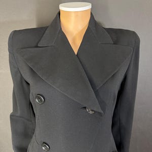 Puede incluir: Un abrigo negro de doble botonadura con cuello ancho y cuatro botones grandes.