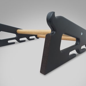 May include: A black wooden rack with a natural wood dowel. The rack has a unique design with cut-out shapes and a curved top. The rack is designed to hold items and has a sturdy base. The rack is made of wood and has a matte finish.