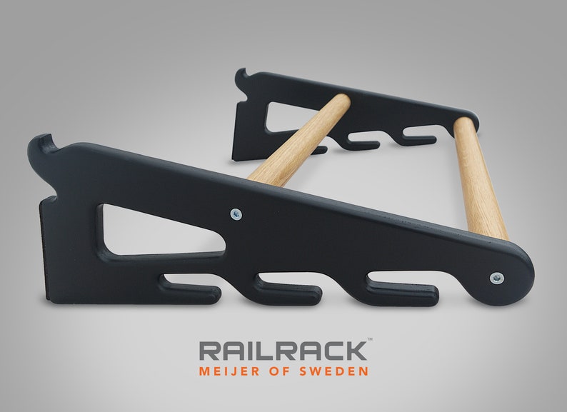 May include: Black wooden rail rack with natural wood dowels. The rack has a unique design with curved edges and multiple hooks for hanging items. The text "RAILRACK MEIJER OF SWEDEN" is printed at the bottom.