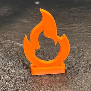 May include: An orange flame-shaped object with a rectangular base. The flame has a stylized design with curved edges and a hollow center. The object is made of a solid material and stands upright.