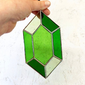 May include: A green and white stained glass geometric ornament shaped like a gemstone. The ornament has a silver frame.