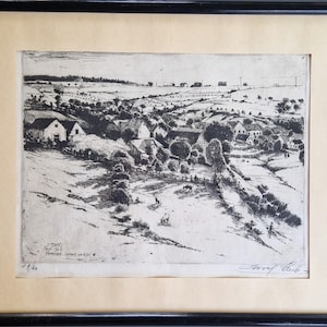 May include: A framed black and white etching of a rural scene. The artwork shows a village with houses, trees, and fields. The print is signed and numbered 19/60. The artwork is mounted on a cream-coloured mount.
