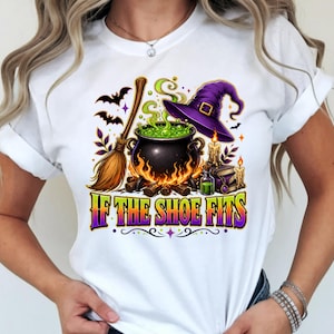Peut inclure: Un t-shirt blanc avec une impression graphique représentant un chaudron noir contenant un liquide vert bouillonnant, un chapeau de sorcière violet, un balai, des bougies et un livre. Le texte "IF THE SHOE FITS" est imprimé en grandes lettres colorées.