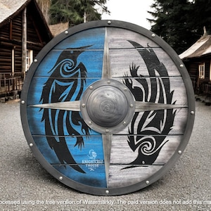 May include: A circular wooden shield with a metal rim and central boss. The shield is split into blue and grey sections, each displaying a black raven design. The shield has a distressed look, possibly indicating a historical or Viking theme.