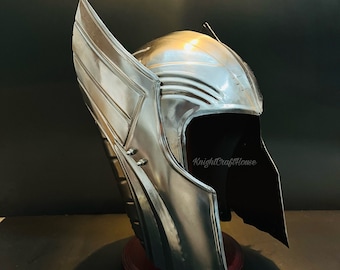 May include: A silver helmet with a winged design. The helmet has a visor and is on a wooden stand. KnightCraftHouse is printed on the helmet.