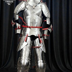 May include: A full suit of polished steel armor with red leather straps. The armor includes a helmet, chest plate, arm and leg protection. The Knightcrafthouse logo is visible on the chest plate. The armor is displayed against a dark background.