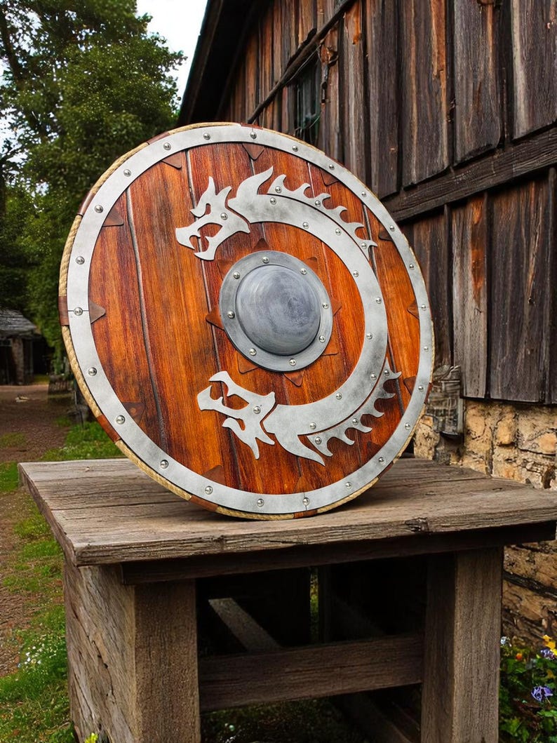 May include: A round wooden shield with a metal rim and a silver dragon design. The shield is resting on a wooden table.