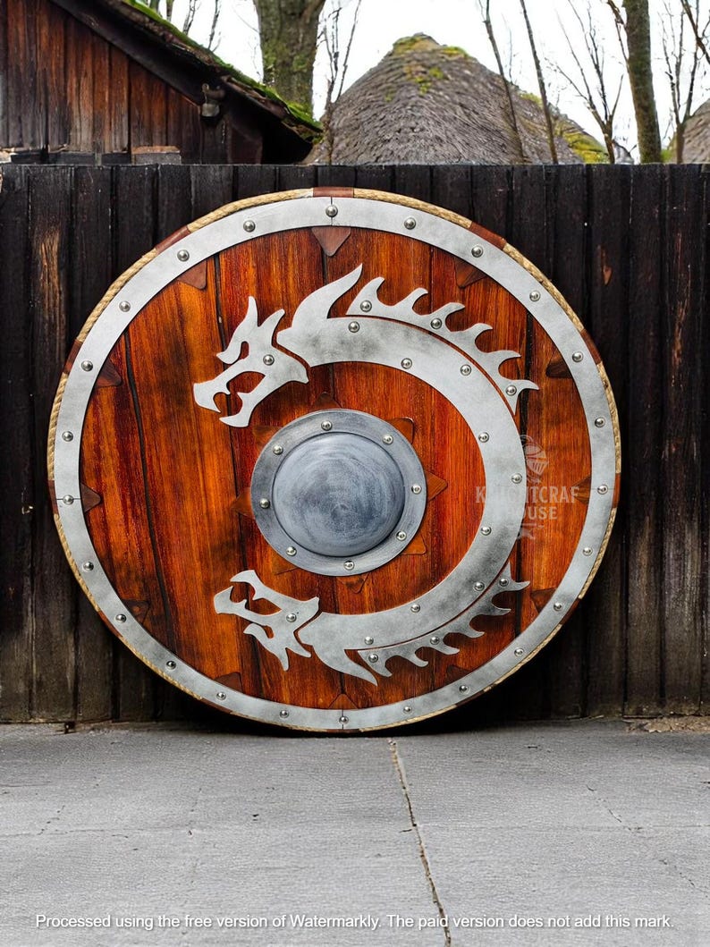 May include: A round wooden shield with a metal rim and a silver dragon design. The shield has a metal boss in the center and is decorated with metal rivets.