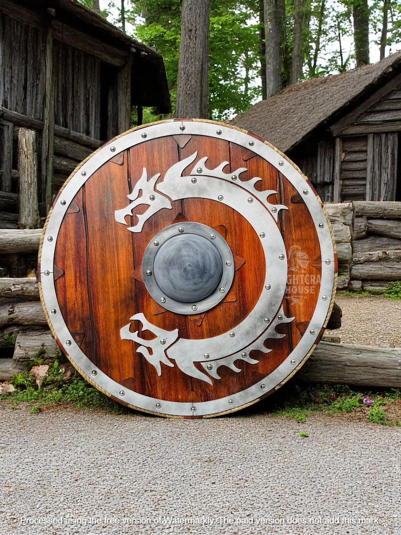 May include: A round wooden shield with a silver dragon design. The shield has a metal rim with rivets and a small metal boss in the center. The shield is leaning against a wooden building.