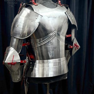 May include: A polished, silver-colored suit of armor, featuring shoulder and arm protection, a chest plate, and a waist guard. Red leather straps and accents are visible. The text "KNIGHTCRAF THOUSE" is printed on the armor.
