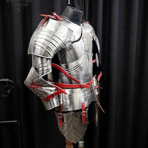 May include: A full suit of polished steel armor with red leather straps and accents. The armor is displayed on a mannequin, showcasing its intricate design and craftsmanship. The Knightcrafthouse logo is visible.