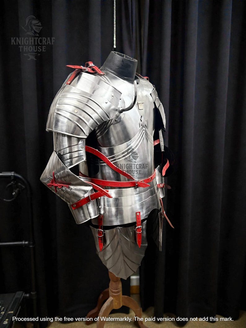 May include: A full suit of polished steel armor with red leather straps and accents. The armor is displayed on a mannequin, showcasing its intricate design and craftsmanship. The Knightcrafthouse logo is visible.