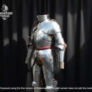 May include: A full suit of polished steel armor, featuring articulated plates and red leather accents. The armor is displayed against a dark backdrop, showcasing the intricate craftsmanship and historical design. The Knightcrafthouse logo is visible.