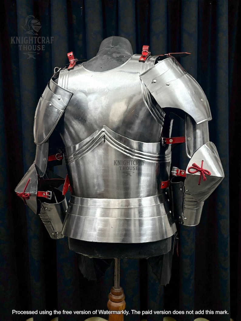 May include: A polished steel medieval armor breastplate and shoulder guards, with red leather straps and accents. The armor is displayed on a mannequin, showcasing its intricate design and craftsmanship. The Knightcrafthouse logo is visible.
