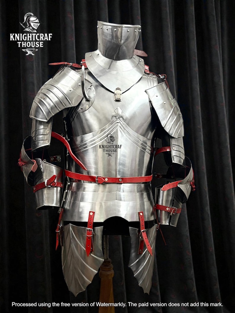 May include: A full suit of polished steel armor with red leather straps and accents. The armor includes a helmet, chest plate, shoulder guards, and leg protection. The armor is displayed on a wooden stand against a dark background. The Knightcrafthouse logo is visible.