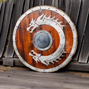 May include: A round wooden shield with a metal rim and two silver dragons on the front. The shield is decorated with metal rivets and has a small round metal boss in the center.