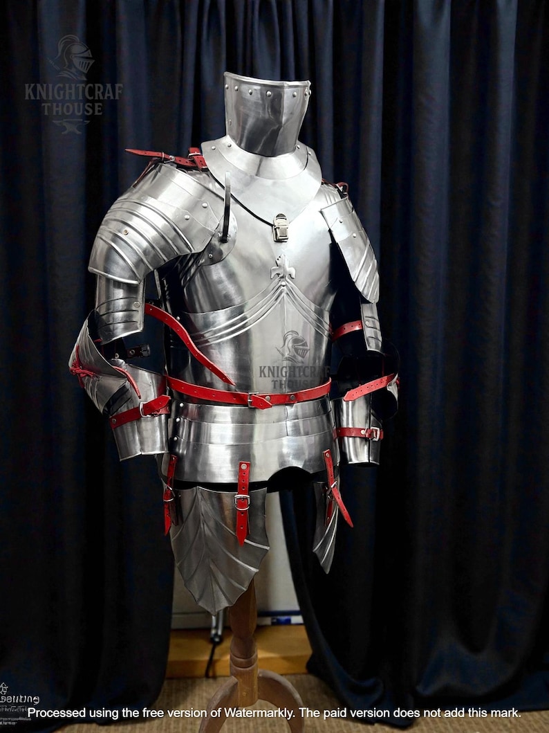 May include: A full suit of polished steel armor with red leather straps and accents. The armor includes a helmet, chest plate, shoulder guards, and leg protection. The armor is displayed on a wooden stand against a dark curtain.