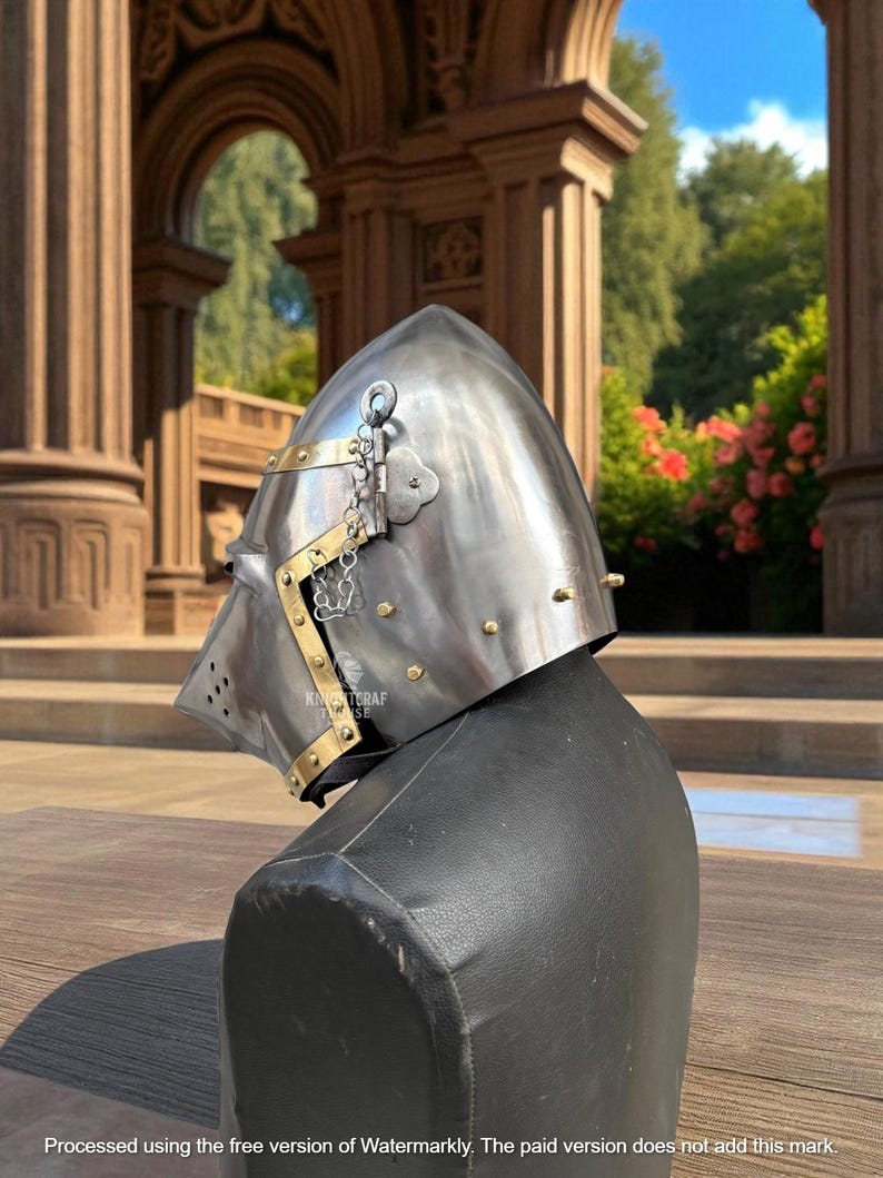 Pu&ograve; includere: Un elmo medievale in acciaio lucido con dettagli in ottone e rivetti. L'elmo presenta una parte superiore appuntita, una visiera con fori di ventilazione e una catena. &Egrave; esposto su un manichino nero, mostrando il suo design storico.