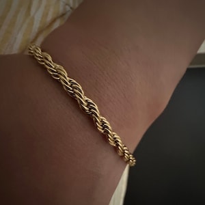 May include: A gold rope chain bracelet on a person's wrist.