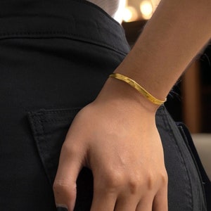 May include: A gold-toned, thin, wavy bracelet on a person's wrist. The bracelet is simple and elegant.