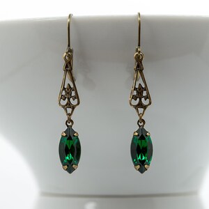 Pu&ograve; includere: Un paio di orecchini color oro antico. Ogni orecchino presenta un design a filigrana con un pendente a forma di marquise in cristallo verde smeraldo. Gli orecchini sono sospesi a un semplice gancio.