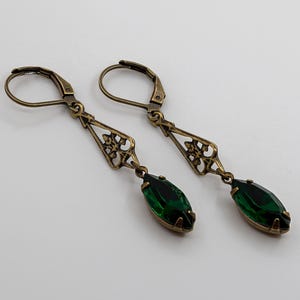 Pu&ograve; includere: Un paio di orecchini in stile antico con finitura bronzo. Ogni orecchino presenta un design a filigrana decorativo e una gemma verde smeraldo a forma di goccia. Gli orecchini hanno una chiusura a leva.