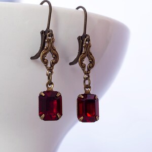 May include: A pair of dangle earrings with a red gemstone and an ornate gold-toned metal design.