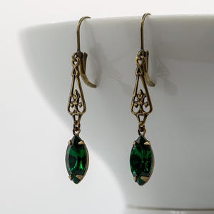 Pu&ograve; includere: Un paio di orecchini color oro antico con un design a filigrana. Ogni orecchino presenta una pietra preziosa verde smeraldo intenso a taglio marquise. Gli orecchini hanno una chiusura a gancio e un'estetica vintage.