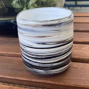 May include: A white ceramic mug with black and brown marbled stripes. The mug is sitting on a wooden surface.