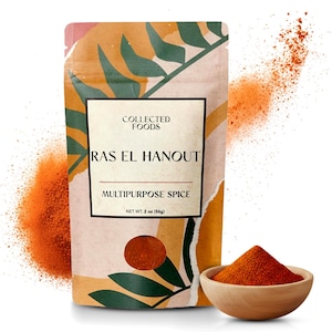 May include: A package of Collected Foods Ras El Hanout multipurpose spice. The package is beige with a colorful design and the text "RAS EL HANOUT" is displayed. A small wooden bowl contains a pile of the spice. Net weight is 2 oz (56g).