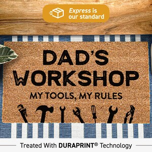 May include: A brown coir doormat with the text "DAD'S WORKSHOP MY TOOLS, MY RULES" in black lettering. The doormat has a row of black tool silhouettes at the bottom.