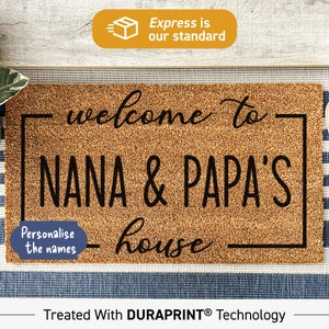 May include: A brown coir doormat with the text "welcome to Nana & Papa's house" in black lettering. The text is framed by a black border. The doormat is on a blue and white striped surface. The text "Personalise the names" is in a white circle on the left side of the doormat. The text "Treated With DURAPRINT® Technology" is at the bottom of the image.