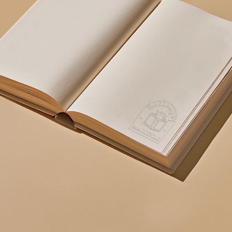 May include: An open book with a white embossed stamp on the cover. The stamp features a book with a flower growing from it and the text "The Library of Maya" around it.