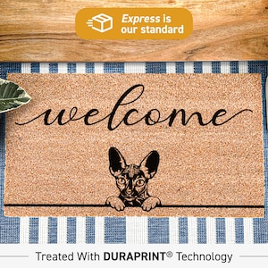 May include: Welcome doormat with a black and white illustration of a Sphynx cat peeking over the top. The doormat is brown and has the word "welcome" written in black cursive. The doormat is treated with DURAPRINT technology.
