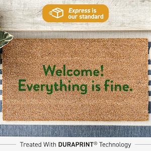 May include: A brown coir doormat with the text "Welcome! Everything is fine." in green lettering. The doormat is treated with DURAPRINT technology.