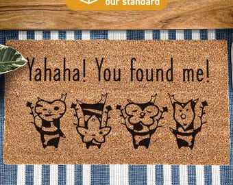 May include: A rectangular tan coir doormat featuring the black printed text "Yahaha! You found me!" above four distinct black illustrations of small, leaf-like forest creatures. The mat is treated with DURAPRINT technology for durability.