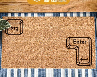 May include: A rectangular tan coir doormat featuring a black printed graphic of an Esc key in the top left corner and an Enter key in the bottom right corner. The mat has a coarse, natural fibre texture and is treated with DURAPRINT technology.