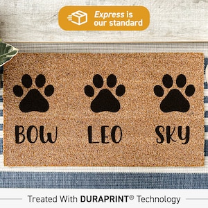 Könnte beinhalten: Eine rechteckige Fußmatte mit brauner Oberfläche, drei schwarzen Pfotenabdrücken und den Namen "BOW", "LEO" und "SKY" in schwarzer Schrift. Die Matte besteht aus einem strukturierten Material und ist für den Außenbereich konzipiert.