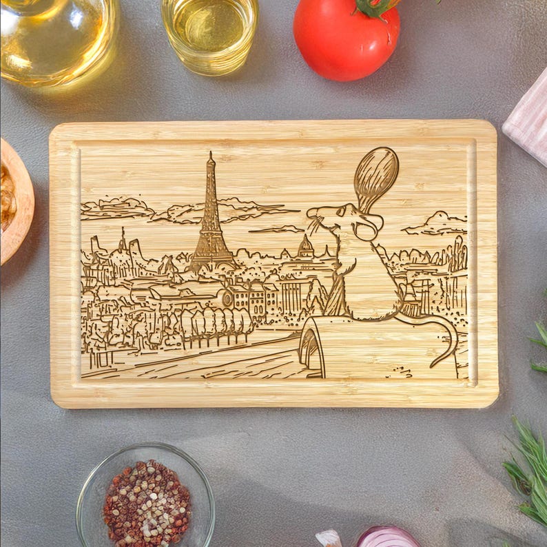Puede incluir: Tabla de cortar rectangular de bamb&uacute; con un dise&ntilde;o grabado con l&aacute;ser de la Torre Eiffel y un chef de dibujos animados. La tabla tiene un borde empotrado y est&aacute; rodeada de ingredientes de cocina.