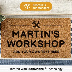 May include: A brown coir doormat with the text "MARTIN'S WORKSHOP" and "ADD YOUR OWN TEXT HERE" in black. The doormat also features a black wrench and hammer symbol.