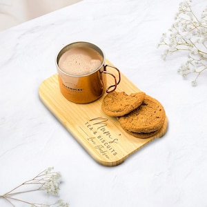 Könnte beinhalten: Eine kupferfarbene Tasse mit Henkel, gefüllt mit einem Getränk, steht auf einem Serviertablett aus Bambus. Das Tablett enthält zwei Kekse und trägt die Gravur "Mum's Tea & Biscuits Love Jackson". Die Tasse ist mit dem Starbucks-Logo versehen.