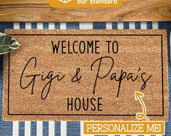 May include: A rectangular tan coir doormat with a black border and the black text "WELCOME TO Gigi & Papa's HOUSE" printed in the center. A yellow arrow points to the text, and a yellow box below contains the white text "PERSONALIZE ME".