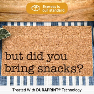 May include: A brown doormat with the text "but did you bring snacks?" printed in black. The doormat is made with DURAPRINT technology.